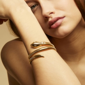 Brazalete flexible con forma de serpiente. Los ojos de las cabezas están adornados con cristales de Swarowski. Metal bañado en oro de 24k.